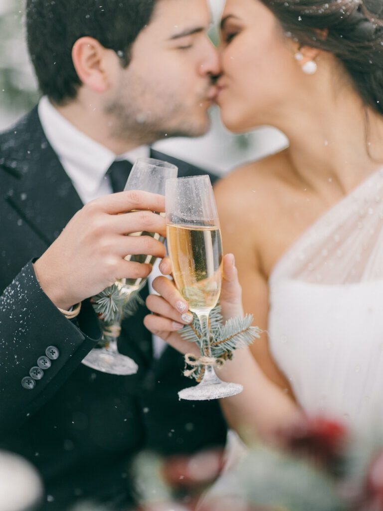 sich küssendes Brautpaar bei der Winterhochzeit mit Sektglas in der hand